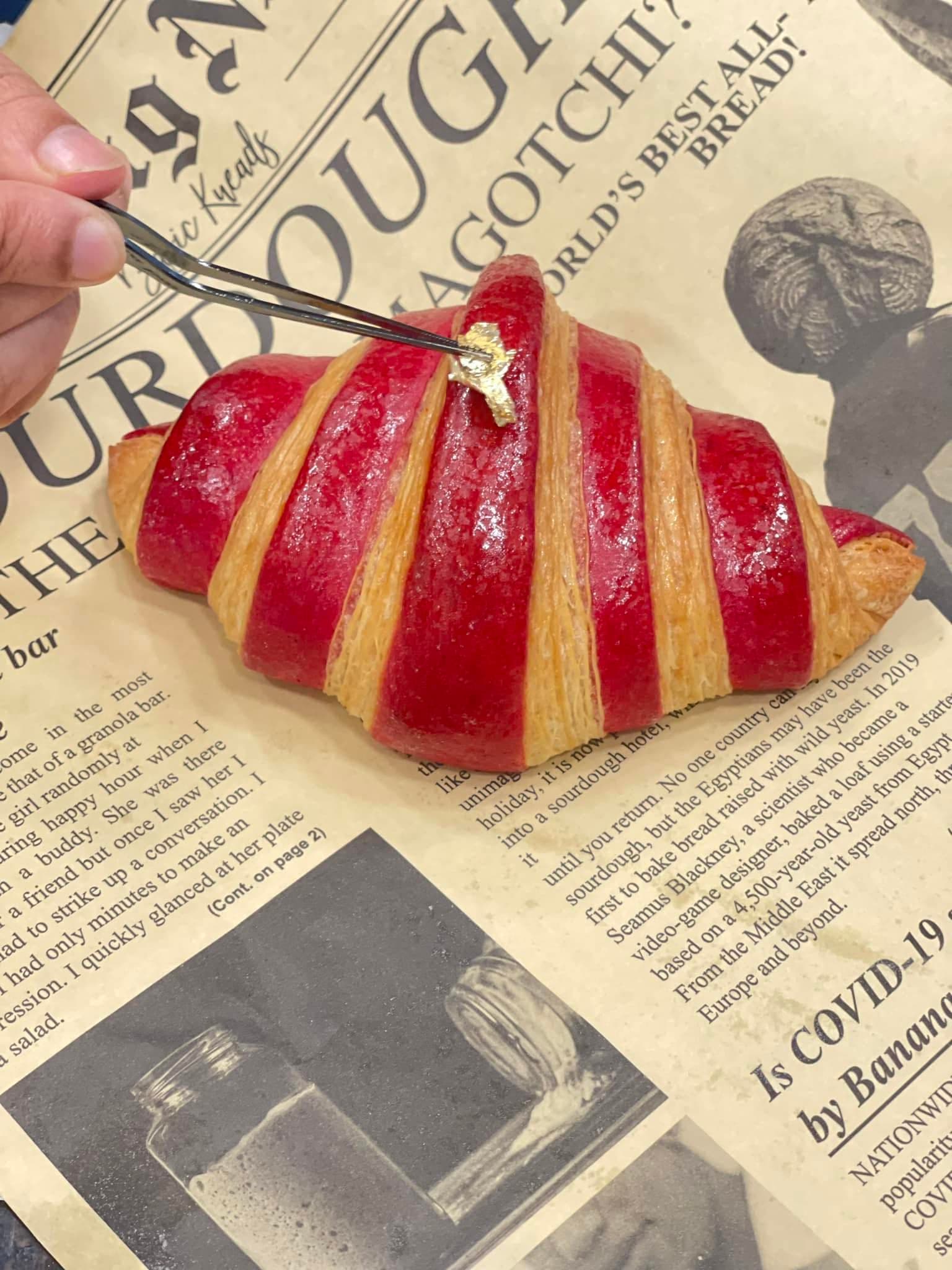 Gold leaf being placed on a striped croissant with tweezers